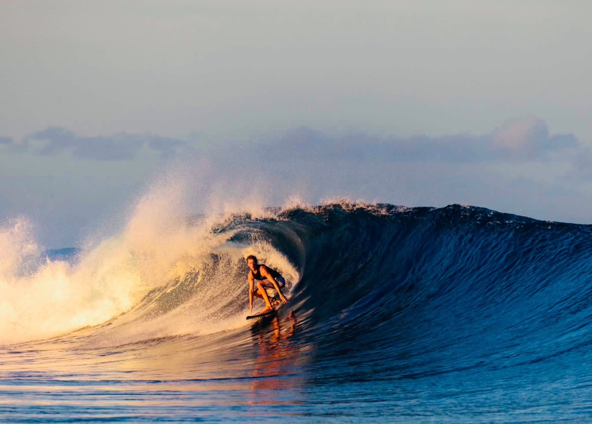 Surfer crouched inside a golden-lit barreling wave